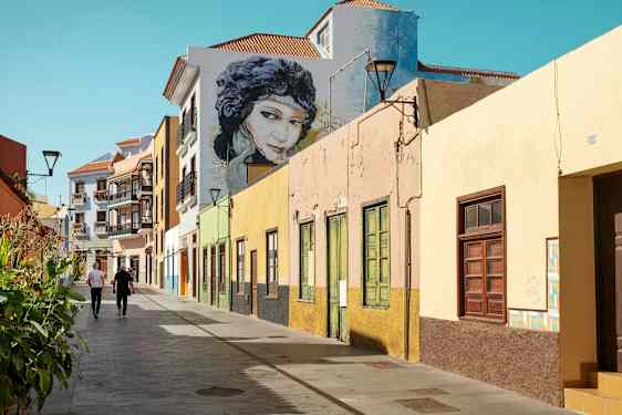 Farverige husfacader langs en gangsti med to personer der går. (AI-genereret tekst)