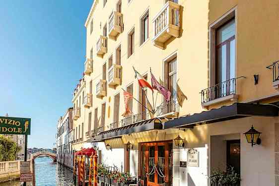 En gul bygning med altaner langs en kanal, med en gangbro i baggrunden. (AI-genereret tekst)