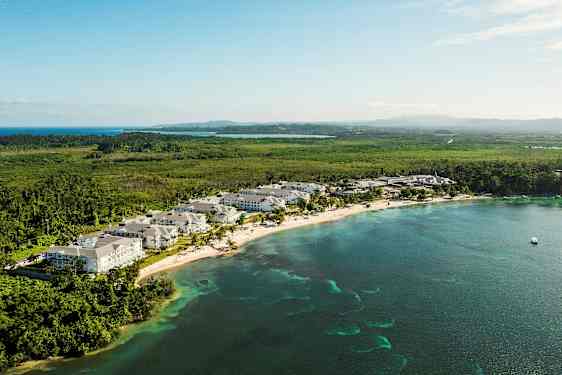 Udsigt over en kyststrækning med ferieområde, omgivet af grønt og hav. (AI-genereret tekst)