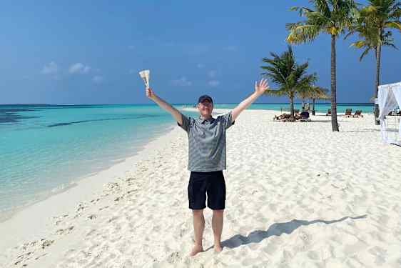 Glad Tomas på hvid sandstrand med turkisblåt hav og palmer