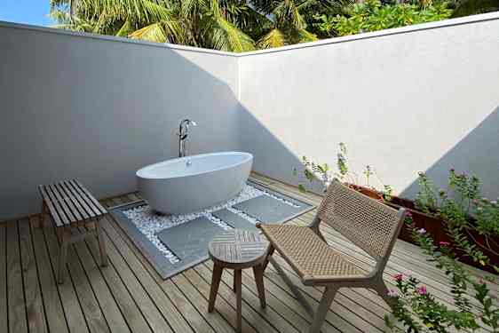 Udendørs badeværelse med badekar, loungegruppe og palmer