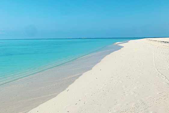 Kridhvid sandstrand med turkisblåt hav og klar himmel