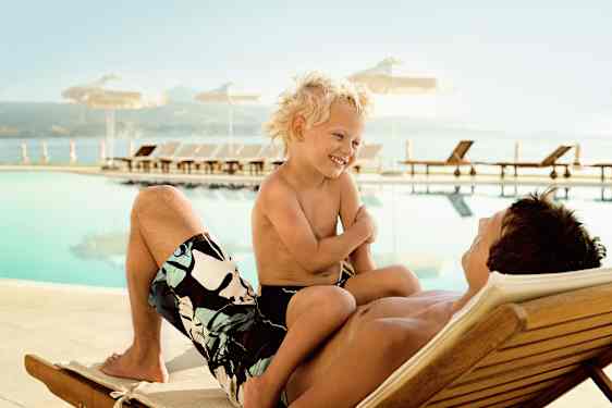 Pappa och son sitter på en solstol vid en pool