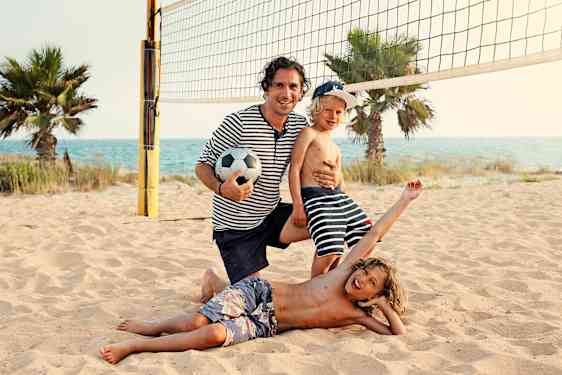Far og sønner spiller volleyball på stranden