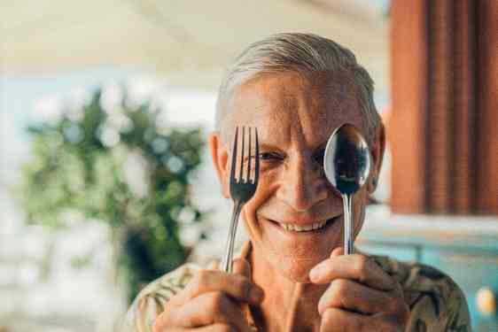 En man håller upp en gaffel och en sked framför ansiktet.