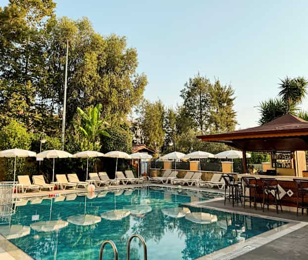 Udendørs pool med liggestole og parasoller ved siden af en bar. (AI-genereret tekst)