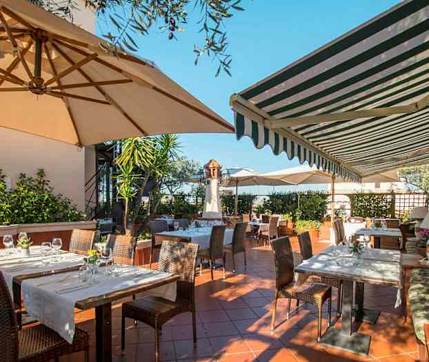 En udendørs servering med borde og stole under parasoller og markiser. (AI-genereret tekst)