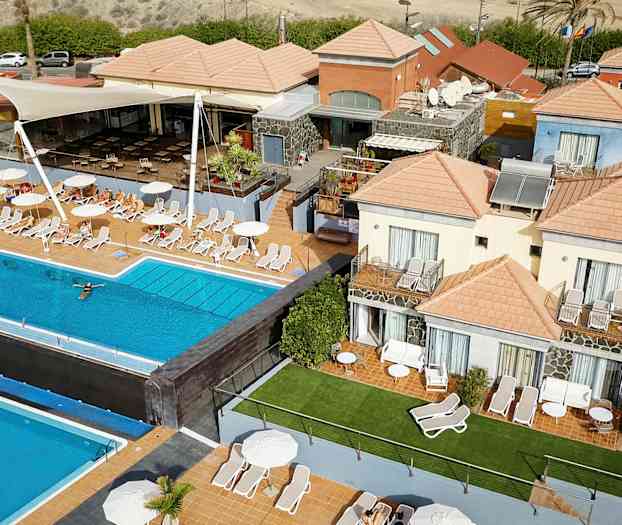 Flere bygninger med orange tage omkring en udendørs swimmingpool og liggestole. (AI-genereret tekst)