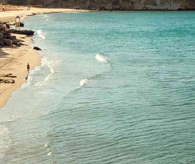 Strand med klart vand og en person, der går langs vandkanten. (AI-genereret tekst)