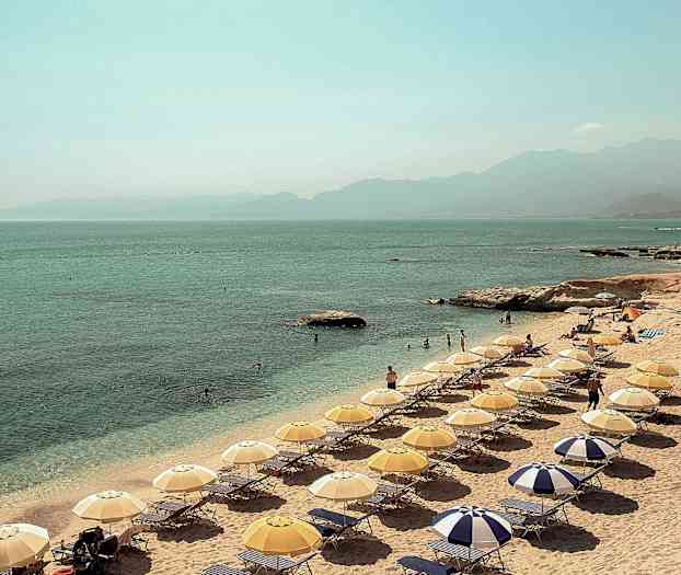 En strand med parasoller og liggestole ved havet. (AI-genereret tekst)