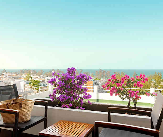 En altan med bord og stole, blomster og havudsigt. (AI-genereret tekst)