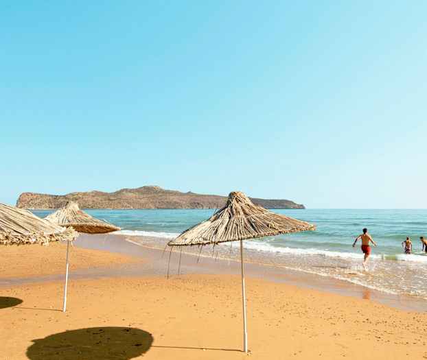 Strand med parasoller af siv og mennesker, der bader i havet. (AI-genereret tekst)