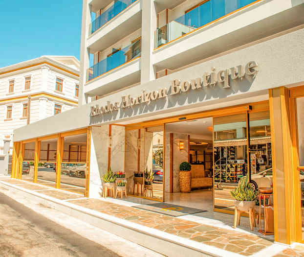 Forsiden af et hotel med navnet Rhodos Horizon Boutique, med glasdøre og planter ved indgangen. (AI-genereret tekst)