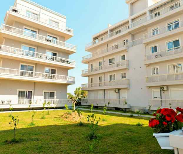 Billede af to moderne flerfamiliehuse med græsplæne og små plantede træer i forgrunden. (AI-genereret tekst)