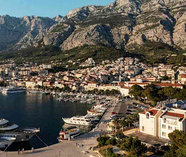 Udsigt over en havn med både og en by med bjerge i baggrunden. (AI-genereret tekst)