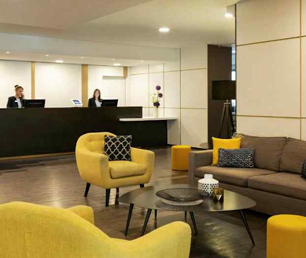 En hotellobby med sofaer og lænestole samt et receptionsområde. (AI-genereret tekst)