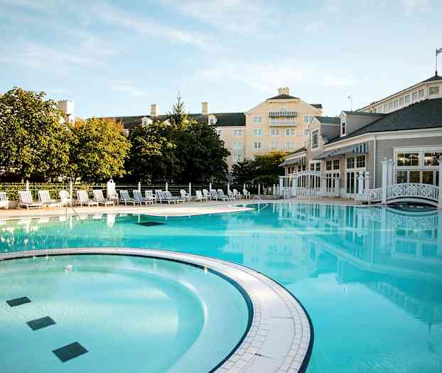 En udendørs pool omgivet af liggestole, bygninger og træer. (AI-genereret tekst)