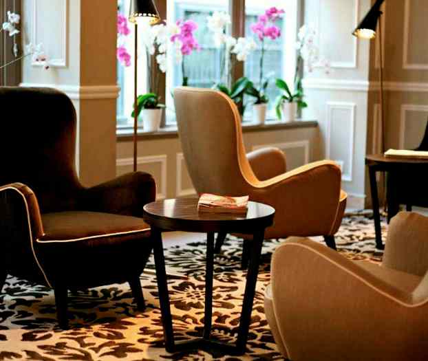 En lounge med komfortable lænestole, et bord og dekorative blomster i vinduerne. (AI-genereret tekst)