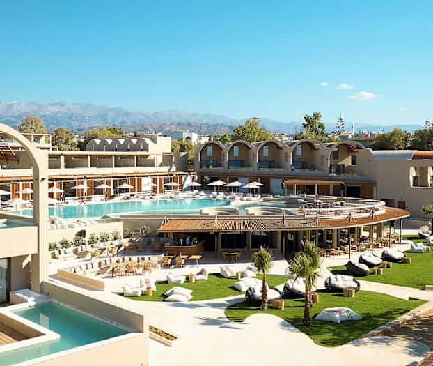 Et moderne hotel med poolområde og frodig have, samt bjerge i baggrunden. (AI-genereret tekst)