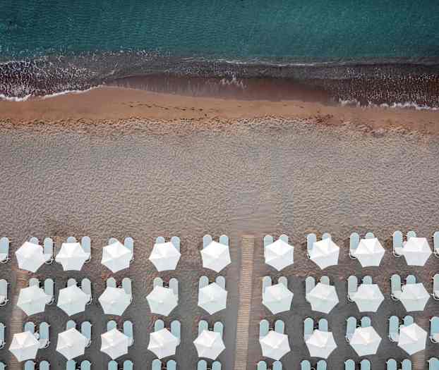 Fugleperspektiv af strand med hvide parasoller og liggestole ved kanten af havet. (AI-genereret tekst)