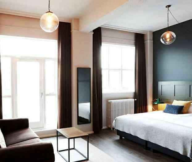 Et hotelværelse med en dobbeltseng, en sofa og et lille sofabord samt store vinduer med gardiner. (AI-genereret tekst)
