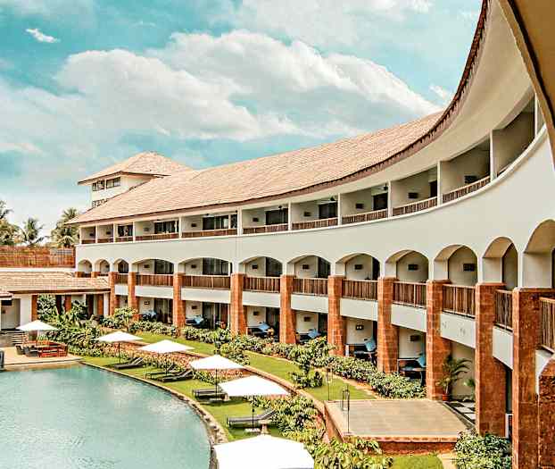 Et udendørs billede af et hotel med en pool, omgivet af grønne områder og hvide parasoller. (AI-genereret tekst)