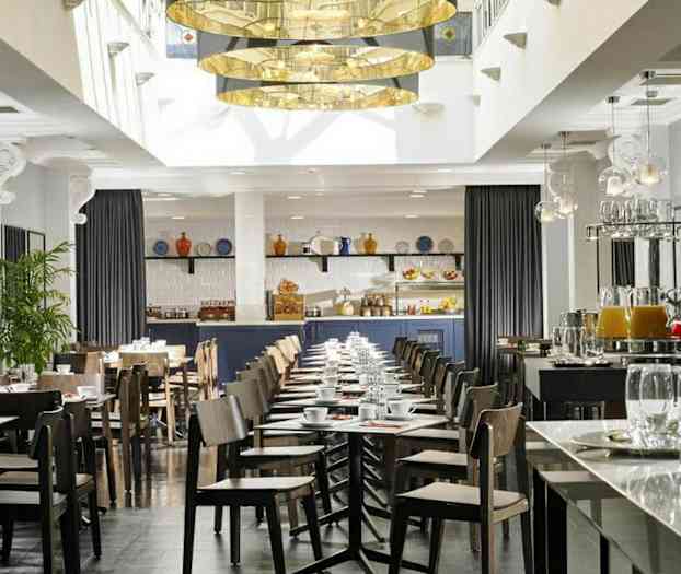 En moderne indrettet café eller restaurant med borde og stole, en serveringsdisk og dekorationer som planter og hængende lamper. (AI-genereret tekst)
