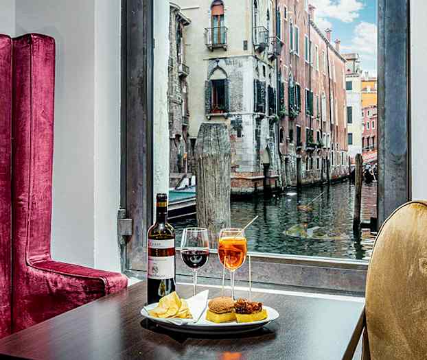 Bord med drikkevarer og snacks, bagved ses en kanal med bygninger. (AI-genereret tekst)