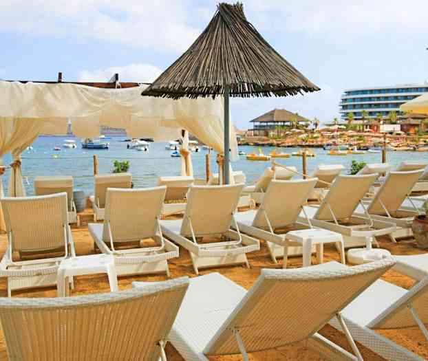 En strand med solsenge foran en rolig bugt med både. (AI-genereret tekst)