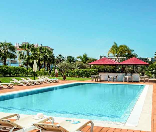 Udendørs pool med liggestole og parasoller, omgivet af grønne områder. (AI-genereret tekst)