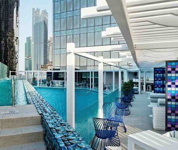 En moderne udendørs pool omgivet af høje bygninger med siddepladser ved siden af. (AI-genereret tekst)