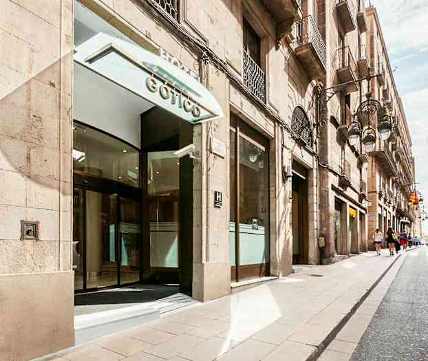 Indgangen til en bygning med glasdøre, beliggende på en gade med bygninger på begge sider. (AI-genereret tekst)