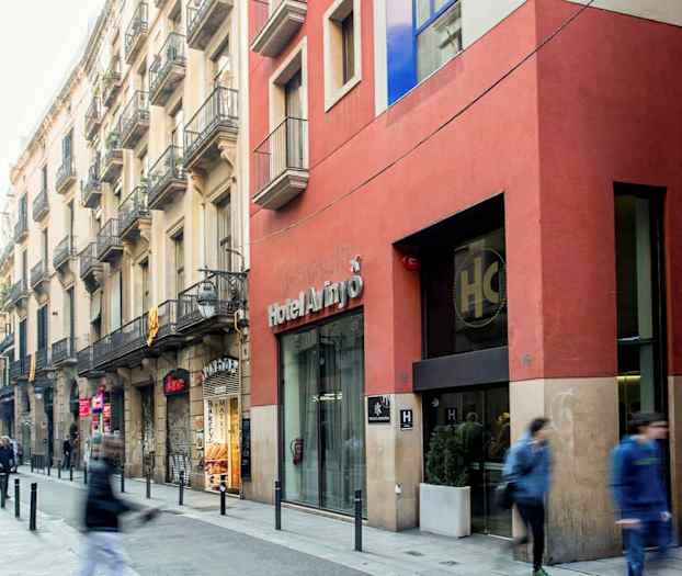 En bygade med mennesker, der går forbi, facader af bygninger og en indgang til et hotel. (AI-genereret tekst)