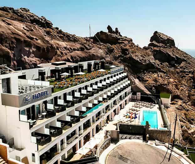 Et hotel beliggende ved en bjergskråning med poolområde og havudsigt. (AI-genereret tekst)