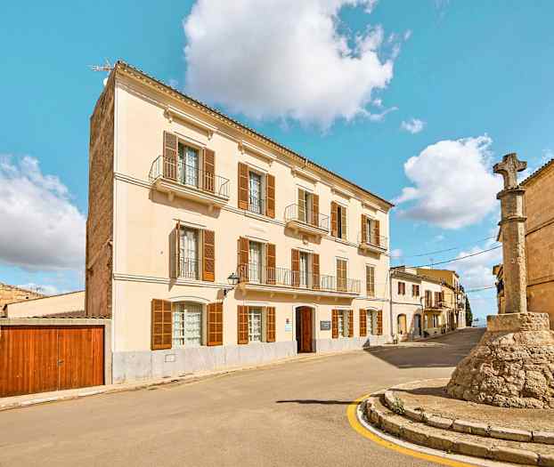 Gade med en bygning med lys facade og en stensøjle med kors. (AI-genereret tekst)