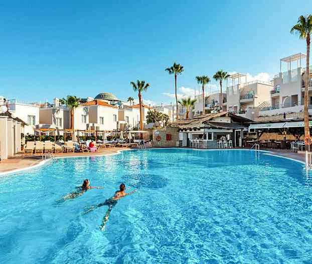 En stor udendørs pool foran hvide bygninger og palmer. (AI-genereret tekst)