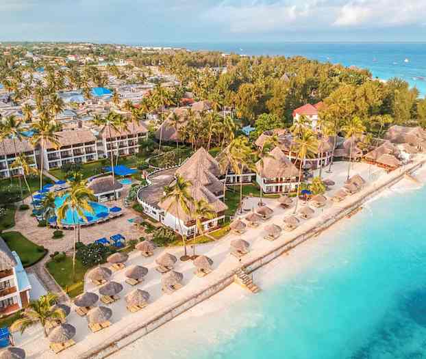 Luftfoto viser en strandresort med tropiske bygninger omgivet af palmer tæt på turkist vand. (AI-genereret tekst)