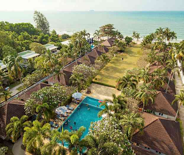 Luftfoto af et feriested med bungalower, pool, palmer og havudsigt. (AI-genereret tekst)