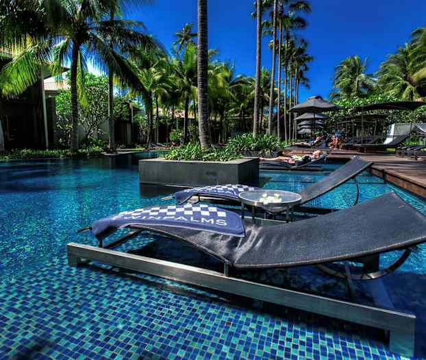 Billede af liggestole ved en pool omgivet af palmer. (AI-genereret tekst)