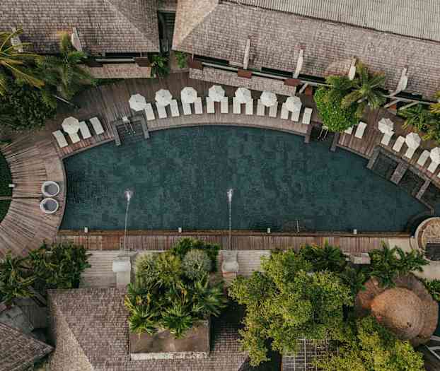 Luftfoto af en pool omgivet af liggestole, parasoller og frodig vegetation. (AI-genereret tekst)