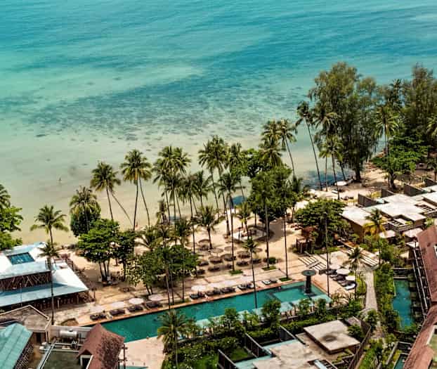 Luftfoto af en strandresort ved havet med palmer, sandstrand og swimmingpools. (AI-genereret tekst)