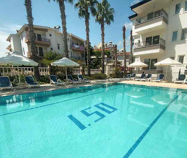 En udendørs swimmingpool omgivet af liggestole og parasoller med lejlighedsbygninger i baggrunden. (AI-genereret tekst)