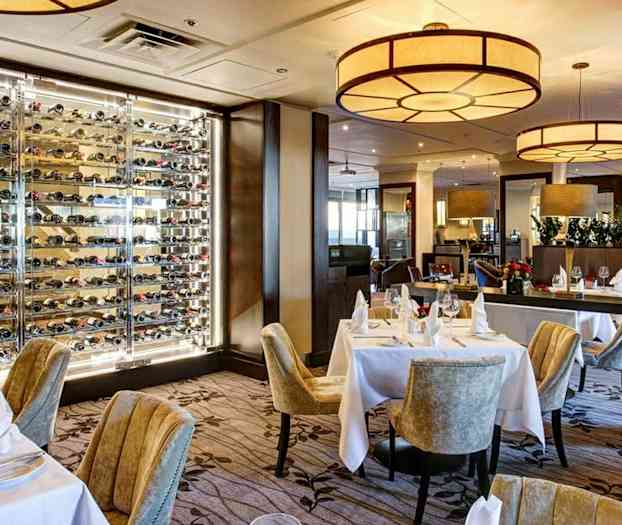 En restaurant med dækkede borde og en væg med vinflasker. (AI-genereret tekst)