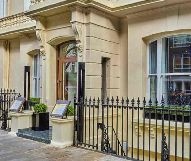 Indgang til en bygning med dekoreret facade og metalhegn. (AI-genereret tekst)