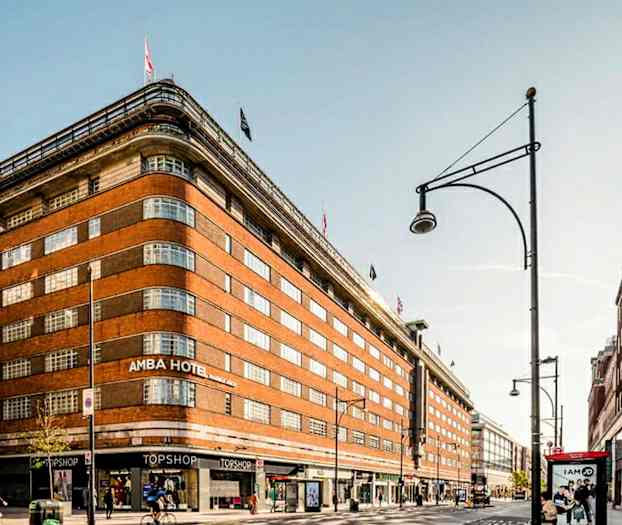 En stor murstensbygning med flag på toppen og butikker i stueetagen. (AI-genereret tekst)