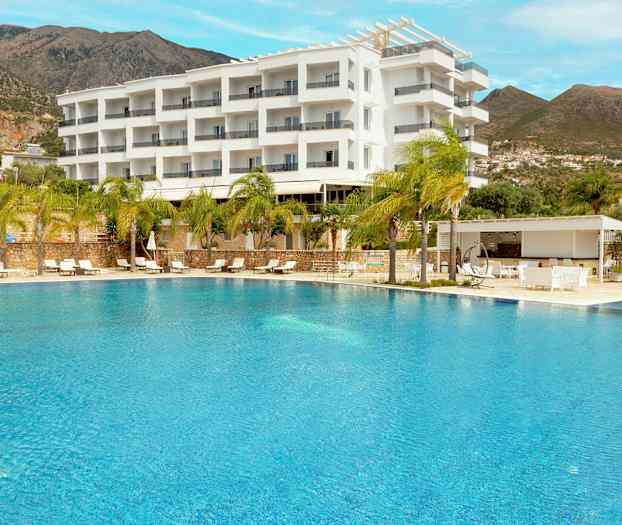 En udendørs pool foran et hotel bygget i en moderne hvid stil, omgivet af palmer og bjerge i baggrunden. (AI-genereret tekst)