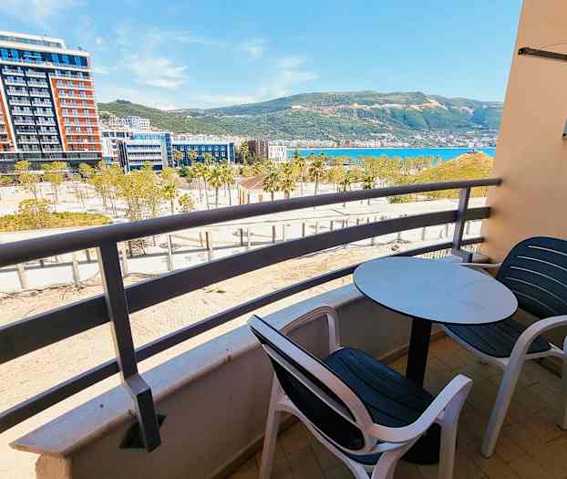 En altan med bord og stole med udsigt over et byggeområde, by og bjerge. (AI-genereret tekst)