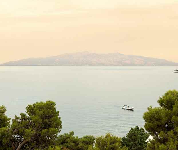 En fjern ø ses over havet med træer i forgrunden og to både på vandet. (AI-genereret tekst)