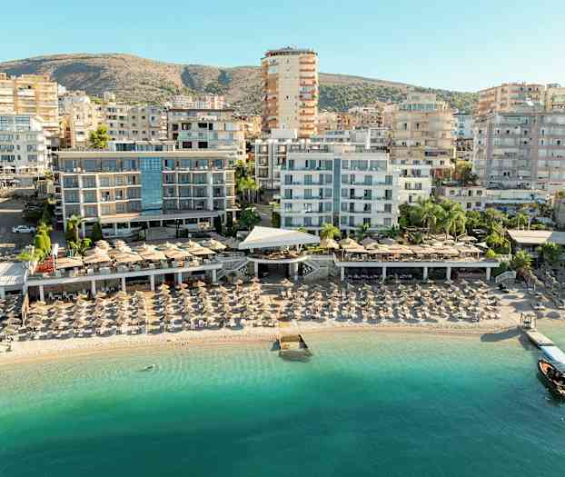 Udsigt over strand med liggestole og hotelbygninger i baggrunden. (AI-genereret tekst)