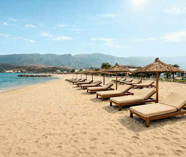 En sandstrand med liggestole og parasoller på række foran havet. (AI-genereret tekst)